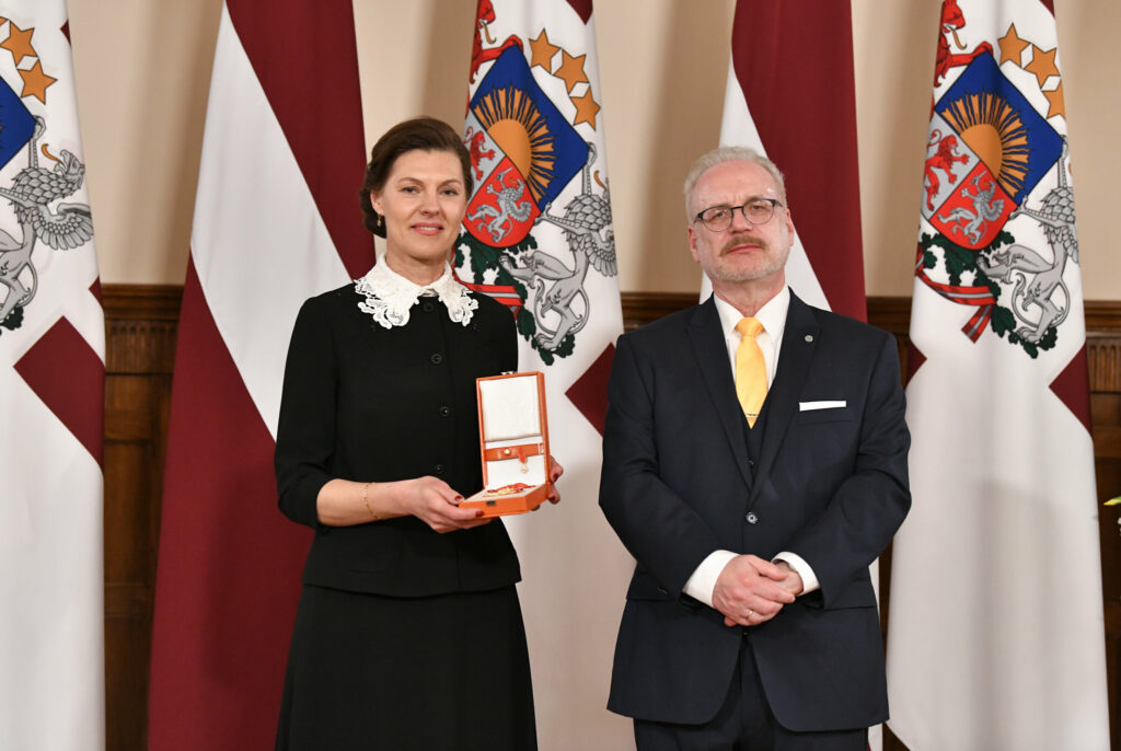 Attēlā (no kreisās) redzama tiesībsarga vietniece Ineta Piļāne, turot rokās Atzinības krustu. Viņai blakus stāv Valsts prezidents Egils Levits. Fonā redzami Latvijas karogi un ģerboņi.