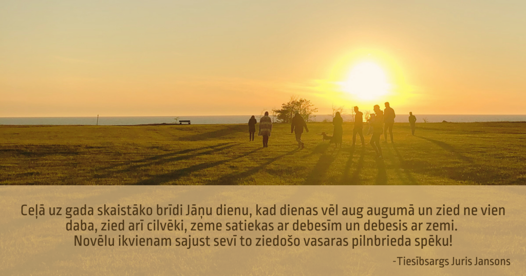 Vasaras saulriets virs jūras, piekrastē vairāki cilvēki un suns. Tekstā: Ceļā uz gada skaistāko brīdi Jāņu dienu, kad dienas vēl aug augumā un zied ne vien daba, zied arī cilvēki, zeme satiekas ar debesīm un debesis ar zemi. Novēlu ikvienam sajust sevī to ziedošo vasaras pilnbrieda spēku! Tiesībsargs Juris Jansons