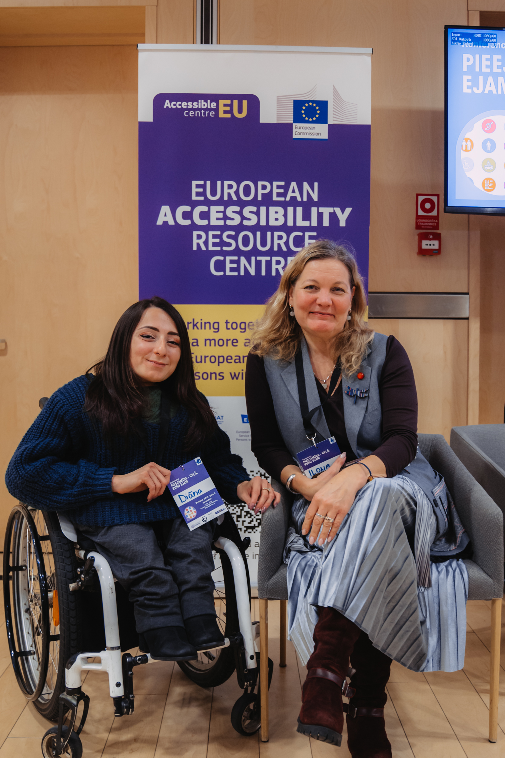 Konferences dalībnieces, divas jaunas sievietes pie European Accessibility resource centre plakāta