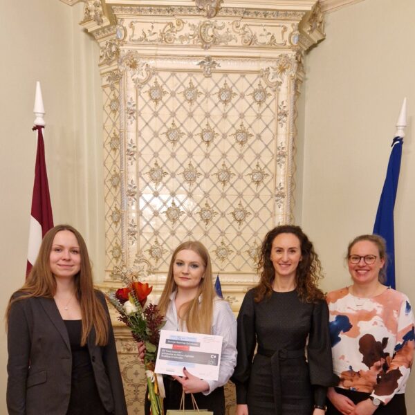 Karina Palkova, Arina Melse un Ieva Šņepste sveic atzinības ieguvēju Anniju Katrīnu Grīnfeldi